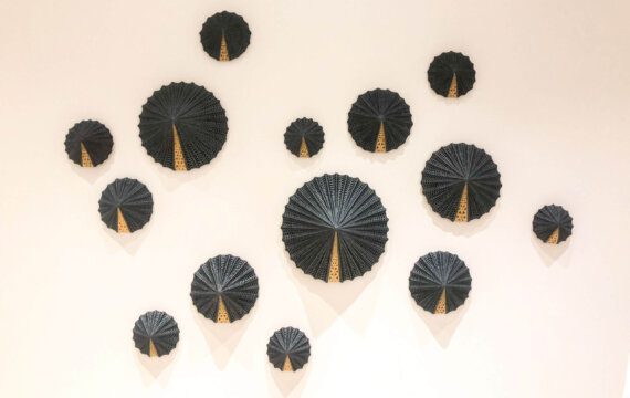 A collection of black, circular, fan-shaped wall decorations with gold accents arranged in a scattered pattern on a plain white wall.