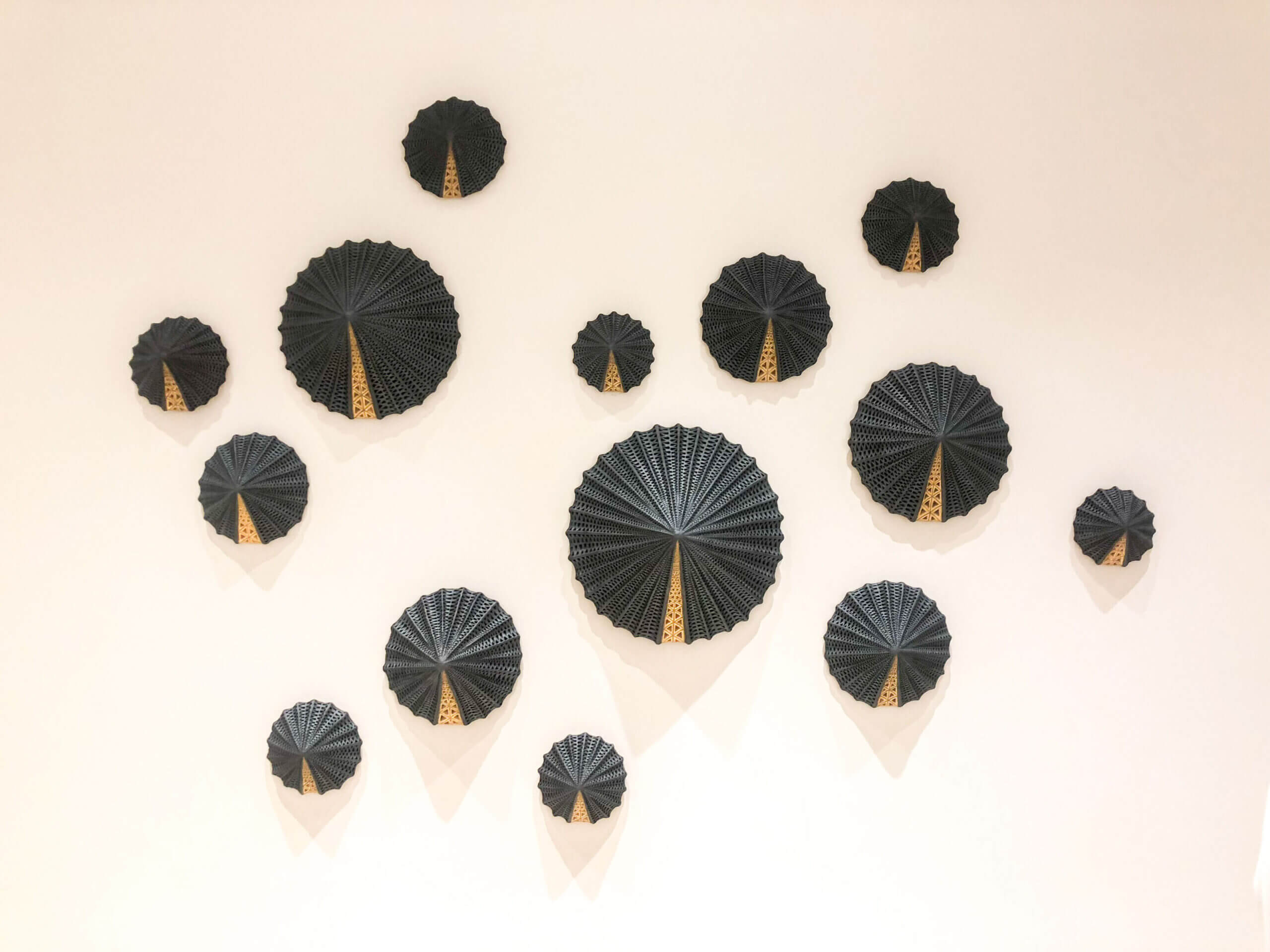 A collection of black, circular, fan-shaped wall decorations with gold accents arranged in a scattered pattern on a plain white wall.